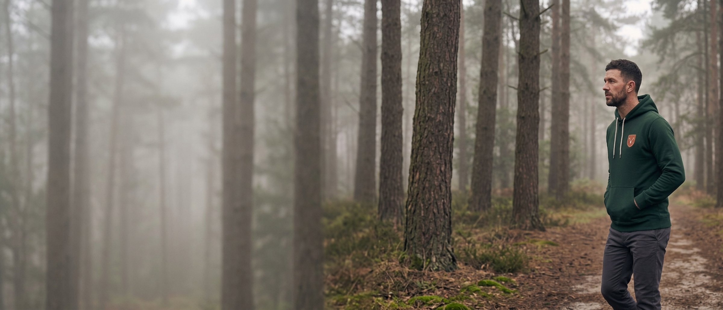 A man in The Delamere Hoodie among tall pines in morning mist